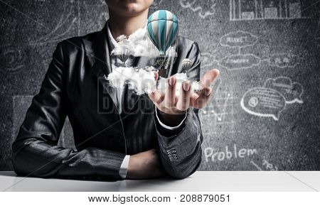 Closeup of business woman in suit presenting flying aerostate among clouds in her palm with business sketches on background. 3D rendering.