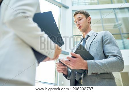 Low angle view of handsome young businessman presenting ideas to female colleague while having informal working meeting at office lobby