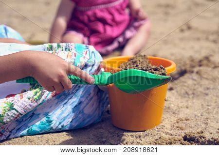 Children's shovel and bucket close-up in the hands of a girl playing in the sandbox.