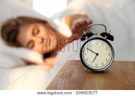 Sleepy young woman stretching hand to ringing alarm willing turn it off. Early wake up, not getting enough sleep, getting work concept