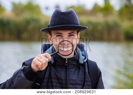 A cheerful young man with a funny face in a hat holds a magnifying glass. Let's celebrate!