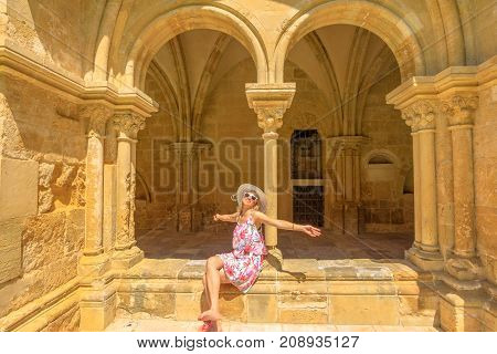 Female tourist enjoying in university town of Coimbra. Freedom woman with open arms at old Coimbra Cathedral or Se Vhelha de Coimbra in a sunny day. Gothic romanesque colonnade on background.