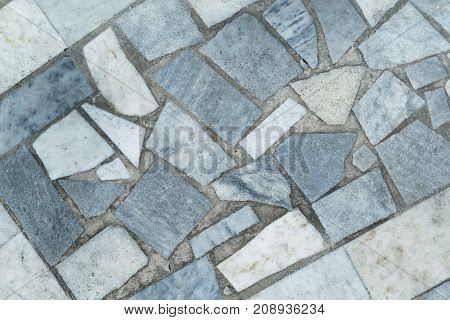 Marble tiles of different shapes laid out on a flat surface. The tiles are rectangular and triangular in shape. Have gray beige and blue. The seams between the tiles filled with concrete or cement.