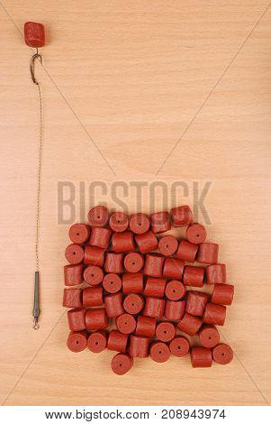 Fishing bait with hook and red pre-drilled halibut pellets for carp fishing isolated on wood background with soft shadow