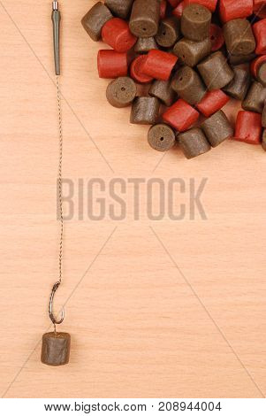 Fishing bait with hook and brown with red pre-drilled halibut pellets for carp fishing isolated on wood background with soft shadow