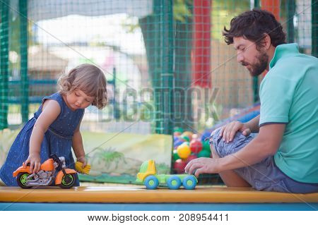 Father play with his toddler daughter in boys games. Two color cars. Family leisure. Loving caring single father. Kid playing with parent.