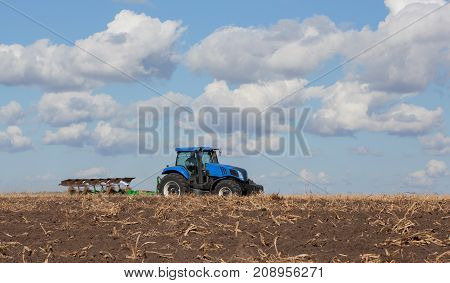 a large blue tractor plowing field against the beautiful sky. Work of agricultural machinery. Harvest