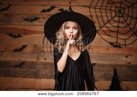 Halloween Witch concept - closeup shot of little caucasian witch child holding index finger at lips asking to keep silence.