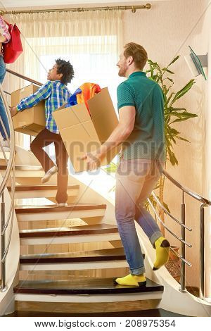 People with boxes walking upstairs. Man and kid indoors.