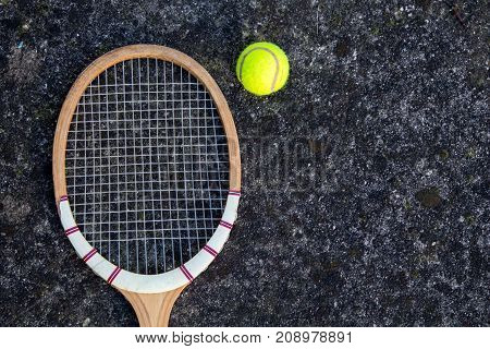 Old vintage wooden tennis racket on isolated stone background with green ball.