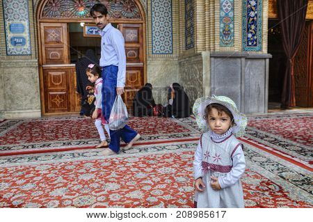 Shiraz Iran - 19 april 2017: Shah Cheragh ShrineOne unknown Iranian girl in the beach hat about 4 years old stands in the courtyard of the mosque against the background of the parishioners.