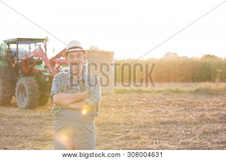 Senior farmer standing at fielf against tractor