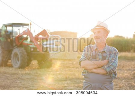 Senior farmer standing at fielf against tractor
