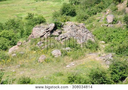 Summer Landscape With Green Plants Around The Old Huge Stones. Wildflowers.