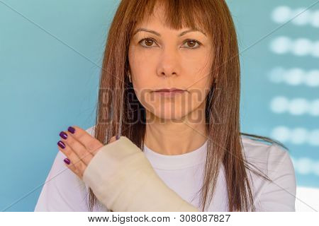 Portrait Middle Aged Woman With Broken Arm Bone In Cast, Plastered Hand On Blue With Sunny Light Bac