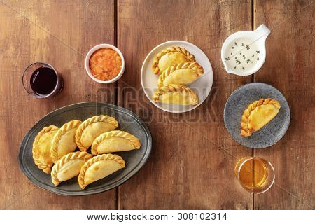 Empanadas With Sauces And Wine, Shot From The Top On A Dark Rustic Wooden Background With A Place Fo