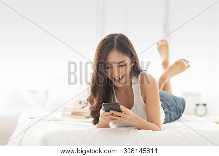 Excited Asian Beautiful Woman While Using Cell Phone Or Mobile Phone While Lying On Her Bed. Cheerfu