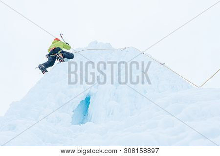 Alpinist Man With Ice Tools Axe In Orange Helmet Climbing A Large Wall Of Ice. Outdoor Sports Portra