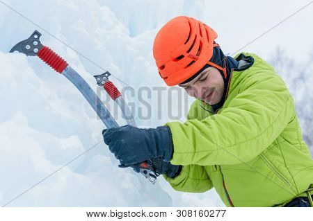 Athletic Alpinist Man In Orange Helmet And Ice Tools Axe Climbing A Large Wall Of Ice. Outdoor Sport