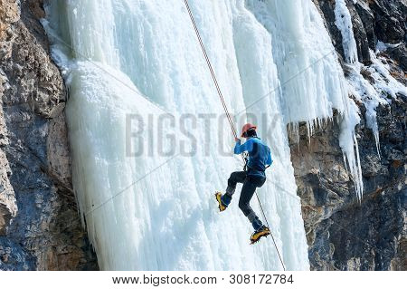 Climber Going Down The Rope With A Frozen Waterfall