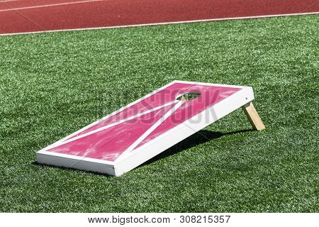 A Red And White Corn Hole Game With White Chalk On It From The Bean Bags On A Green Turf Field.