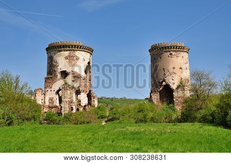 Two Old Destroyed Abandoned Brick Towers Among Green Grasses And Trees In Early Spring.