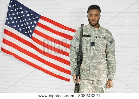 American Male Ranker Looking At Camera, Standing Near Brick Wall And National Flag. Young Solider We