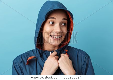 Cheerful young girl wearing raincoat standing isolated over blue background, posing