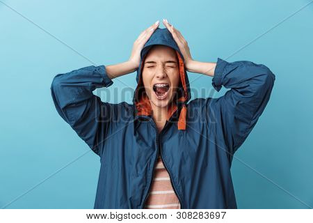 Cheerful young girl wearing raincoat standing isolated over blue background, posing, screaming