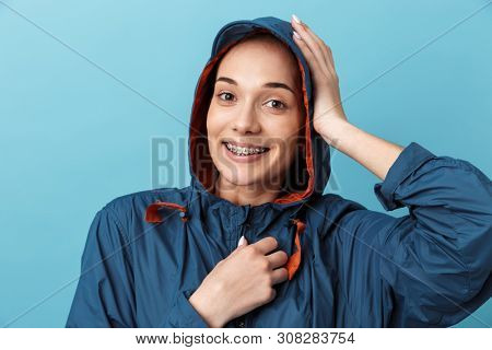 Cheerful young girl wearing raincoat standing isolated over blue background, posing