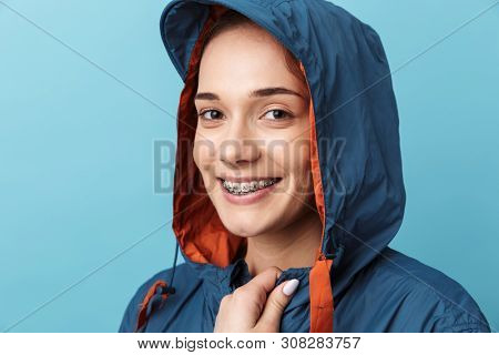 Cheerful young girl wearing raincoat standing isolated over blue background, posing