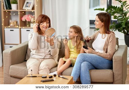 family, generation and female concept - portrait of smiling mother, daughter and grandmother with cosmetics doing make up at home