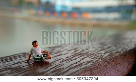 Mini Figure Toy Old Man Sit At Scratch Wooden Balcony At River Side With Copy Or Negative Space For 