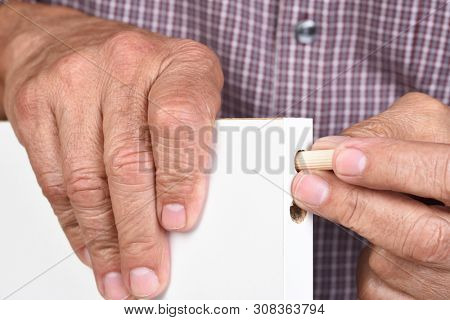Closeup of a man assembling a DIY piece of furniture. The worker is inserting a wooden dowel into a pre-drilled hole.
