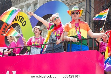 2018 JUNE 24 NEW YORK: NYC Pride March participants wearing pink tshirts wave rainbow flags while riding on the TMobile float on the 5th Ave parade route.
