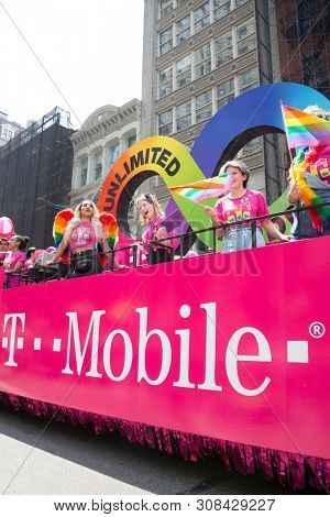 2018 JUNE 24 NEW YORK: NYC Pride March participants wearing pink tshirts wave rainbow flags while riding on the TMobile float on the 5th Ave parade route.