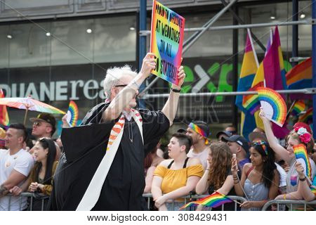2018 JUNE 24 NEW YORK: NYC Pride March participant holds a rainbow sign that says Proud To Officiate At Weddings In All 50 States on the 5th Ave parade route.