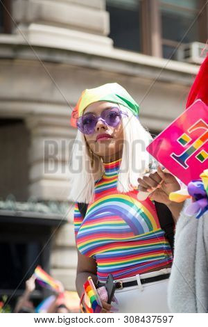 2018 JUNE 24 NEW YORK: NYC Pride March participant wearing big sunglasses and a rainbow tshirt outfit walks along the 5th Ave parade route.
