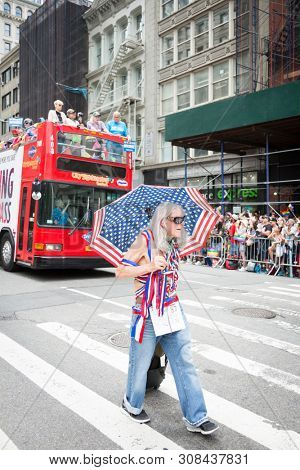 2018 JUNE 24 NEW YORK: NYC Pride March participant walks with an American Flag umbrella at 23rd St and 5th Ave on the parade route.