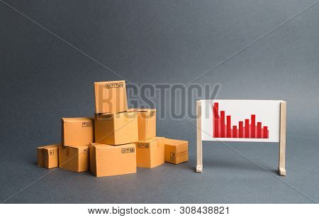Stack Of Cardboard Boxes And A Stand With Information Chart. Rate Growth Of Production Of Goods And 