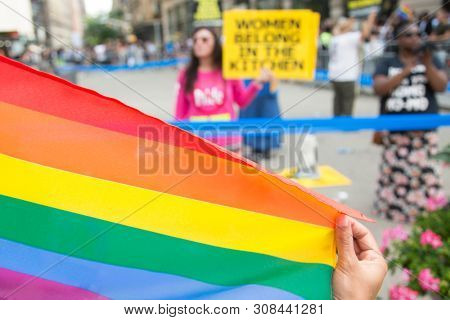 2018 JUNE 24 NEW YORK: Pride March spectator holds a rainbow flag in front of an anti-Pride protestor holding a sign that says Women Belong In The Kitchen on 23rd St at 5th Ave at the NYC Pride March.