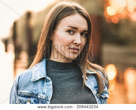 Portrait Of The Attractive, Slender, Beautiful Young Caucasian Blonde Girl In A Jeans Jacket. Smilin