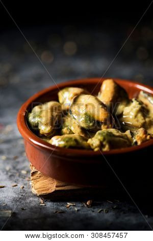 closeup of an earthenware plate with mejillones al curry, spanish curried mussels, on a stone surface