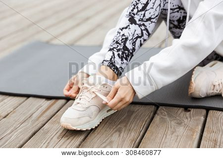 Close up of a sportswoman tying shoelace while sitting on a fitmess mat outdoors