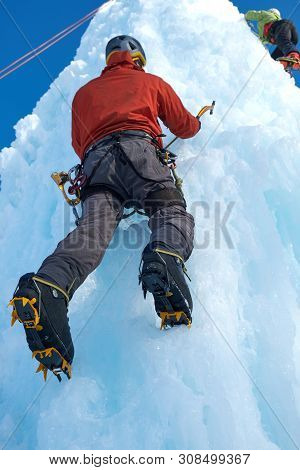 Alpinist Man With Ice Tools Axe Climbing A Large Wall Of Ice. Ou