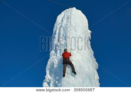 Alpinist Man With Ice Tools Axe Climbing A Large Wall Of Ice. Ou