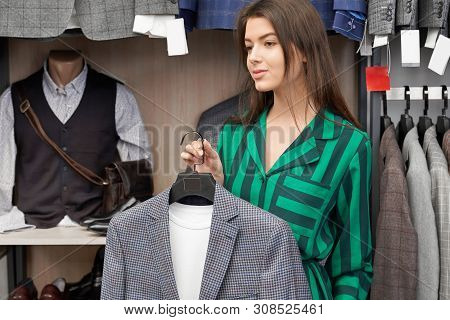 Row Of Male Suit Jackets On Hangers And Mannequin. Young, Pretty Shop Consultant Holding Stylish Mal
