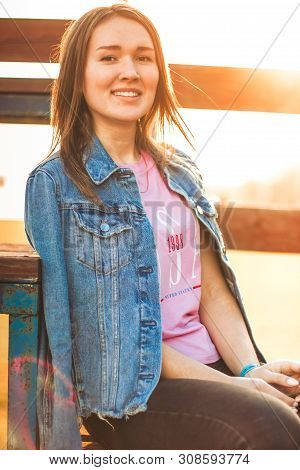 Portrait Of The Attractive, Slender, Beautiful Young Caucasian Blonde Girl In A Jeans Jacket And Pin