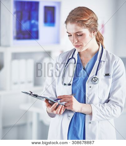 Young Woman Doctor Is Standing With Board With Clipboard Smilin