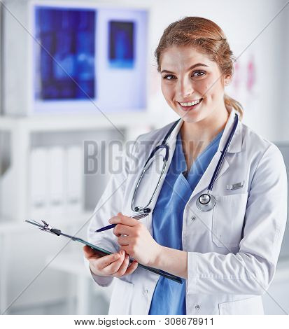 Young Woman Doctor Is Standing With Board With Clipboard Smilin
